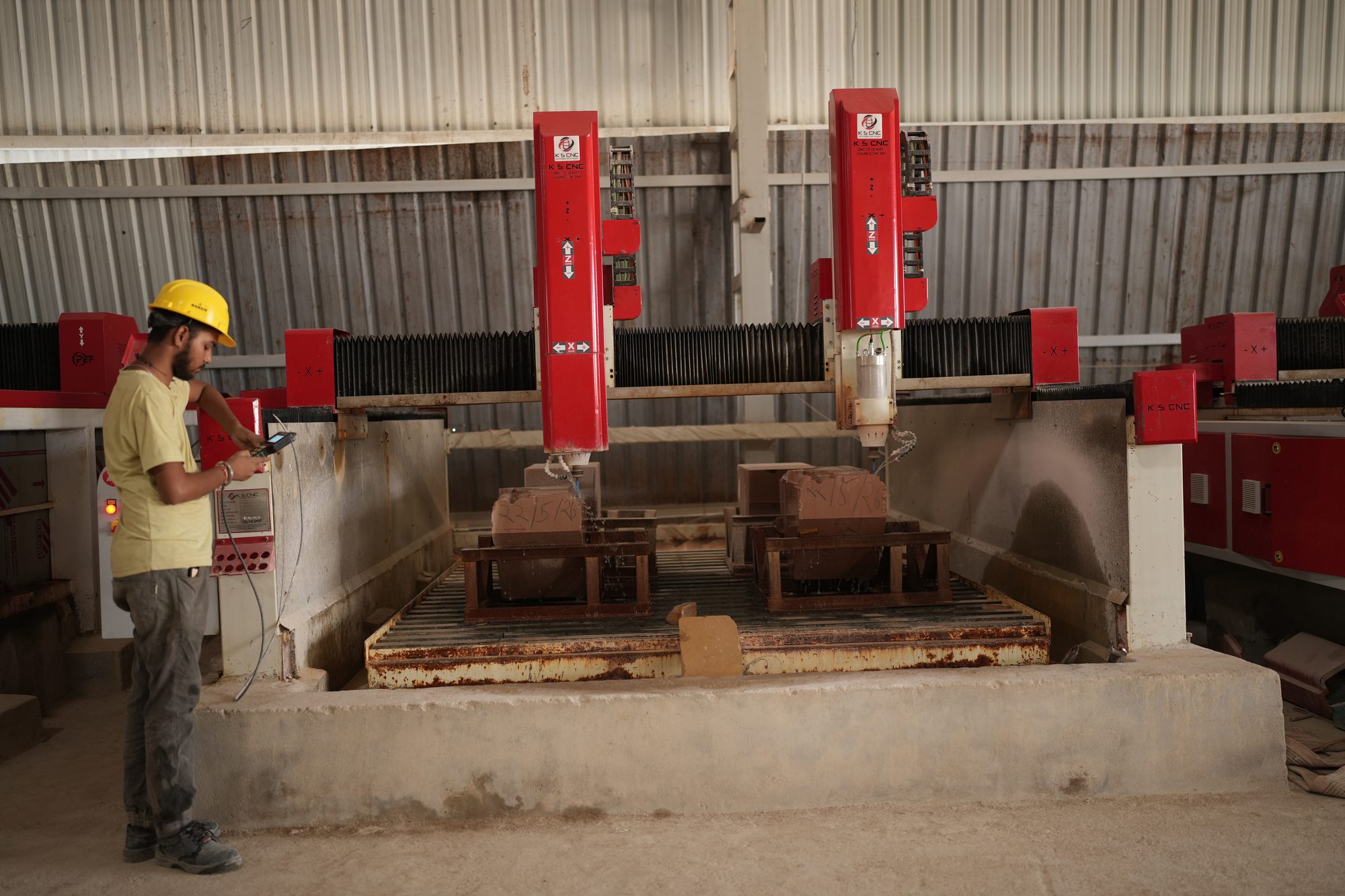 Operator running a red CNC bridge over a sandstone block